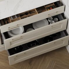 an open drawer with dishes in it on a wooden floor next to a counter top