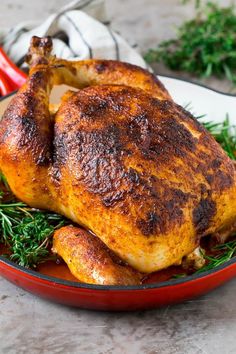 a roasted chicken in a red pan with fresh herbs on the side, ready to be cooked