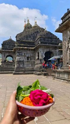 a person holding up a bowl with flowers in front of an old building on a sunny day