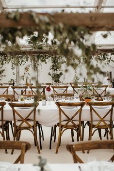 tables and chairs are set up for an outdoor wedding reception with greenery hanging from the ceiling