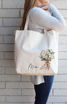 a woman holding a white bag with flowers on it and the word mia written in cursive writing