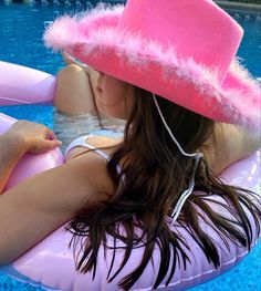 a woman wearing a pink hat sitting on an inflatable raft near a swimming pool