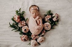 a baby wrapped in a blanket surrounded by flowers and greenery on a white sheet