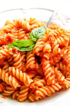 a white plate topped with pasta covered in tomato sauce and basil garnished with a green leaf