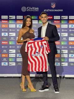 two people standing next to each other holding a red and white soccer jersey with an american flag on it