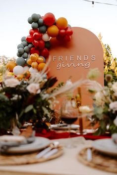 the table is set with plates, silverware and colorful balloons on top of it