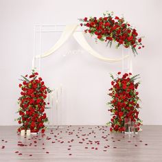 red roses and greenery decorate an arch for a wedding ceremony at the end of a wooden floor