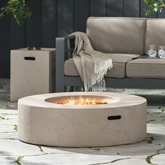 an outdoor fire pit sitting on top of a stone floor next to a couch and table