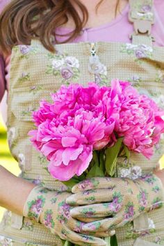 a woman wearing gloves holding a bouquet of pink flowers in her hands with the other hand on her hip