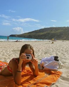 a woman laying on top of a beach holding a camera