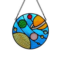 a stained glass sun catcher hanging from a chain on a white background with space and planets in it