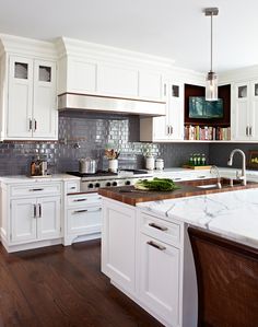 a large kitchen with white cabinets and marble counter tops, along with dark wood flooring