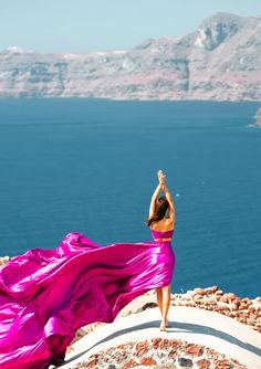 a woman in a pink dress standing on top of a cliff