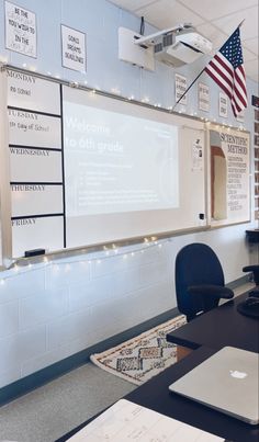 an empty classroom with laptops on the desk and american flag hanging from the wall