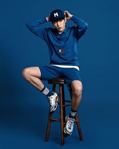 a young man sitting on top of a stool wearing a baseball cap and blue sweatpants