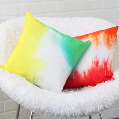 two colorful pillows sitting on top of a white chair