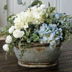 white and blue flowers are in an old metal pot on a table with wood planks