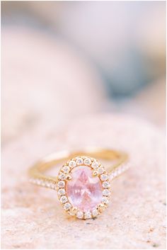 an engagement ring with a pink stone in the center and white diamonds around it, on top of a rock