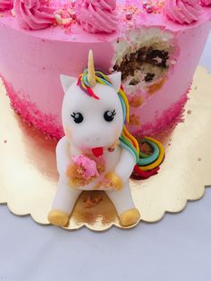 a pink cake with a unicorn figurine next to it