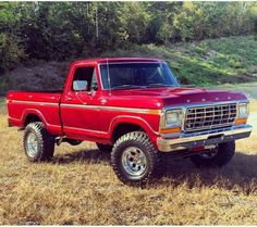 a red pick up truck parked on top of a dry grass field next to trees