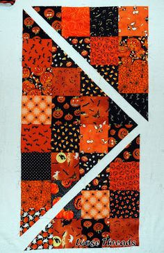 an orange and black patchwork quilt hanging on a white wall next to a pair of scissors