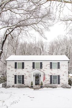 a white brick house with black shutters in the snow