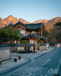 two people standing in front of a building with mountains in the background