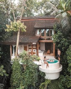 two people are sitting on the edge of a pool in front of a small house