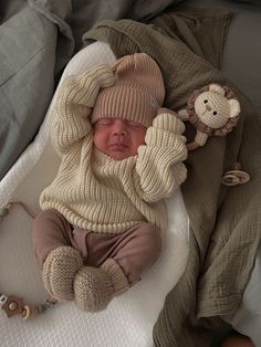 a baby in a knitted outfit laying on top of a bed next to a stuffed animal