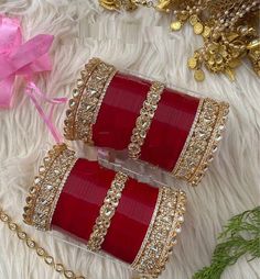 two red and gold bracelets sitting on top of a white fur covered floor next to a pink flower