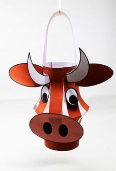 an origami cow head hanging from a string on a white background with one eye open