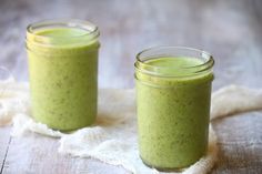 two jars filled with green smoothie sitting on top of a white cloth covered table