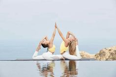 two women doing yoga in front of the ocean