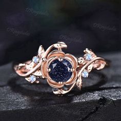 a blue diamond ring on top of a black stone surface with leaves and stones around it