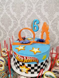 a birthday cake decorated with hot wheels and stars on top is surrounded by cupcakes