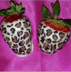 two chocolate covered strawberries are sitting on a pink surface with green leaves and brown spots