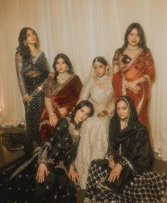 a group of women sitting next to each other in front of a white wall with curtains