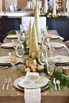 the table is set for christmas dinner with silver and gold decorations on top of it