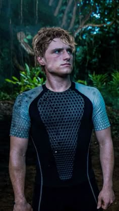 a young man standing in the woods wearing a wet suit