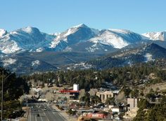 the mountains are covered in snow as traffic passes by on an empty road through town