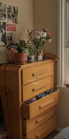 a wooden dresser with drawers and flowers on top in a room next to a window