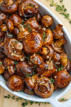 a white dish filled with cooked mushrooms and garnished with herbs