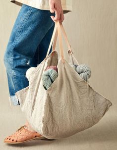 a person holding a bag with balls of yarn in it's handles and feet