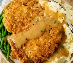 chicken with gravy on top of mashed potatoes and green beans in a white bowl