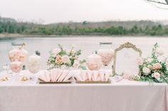 a table topped with lots of pink flowers and vases filled with flowers next to a lake