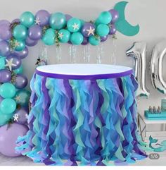 a birthday party with balloons, streamers and mermaid decorations on the wall behind it