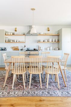 a dining room table and chairs in front of an open kitchen area with shelves on the wall