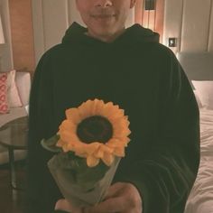 a man in a black hoodie holding a sunflower