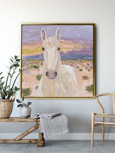 a painting of a white horse is hanging on the wall next to a chair and potted plant