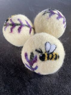 three wool balls with embroidered bees on them sitting on a black tablecloth covered surface